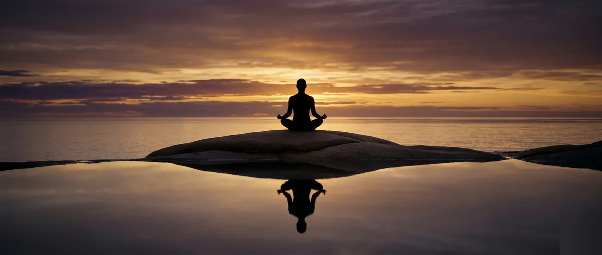 Meditation silhouette at golden sunset over still ocean water