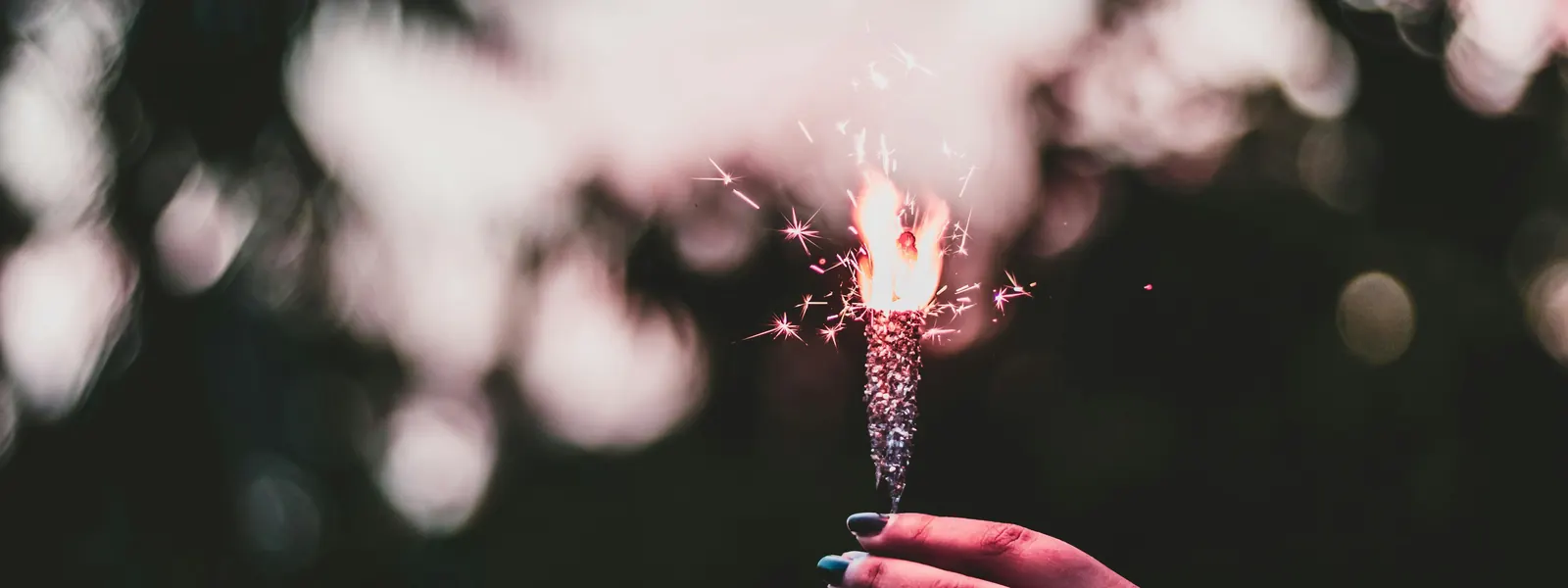A hand holding a lit sparkler against soft, blurred lights